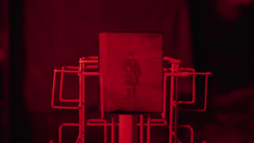 A gloved hand places a developing photograph on a rack with red light glowing