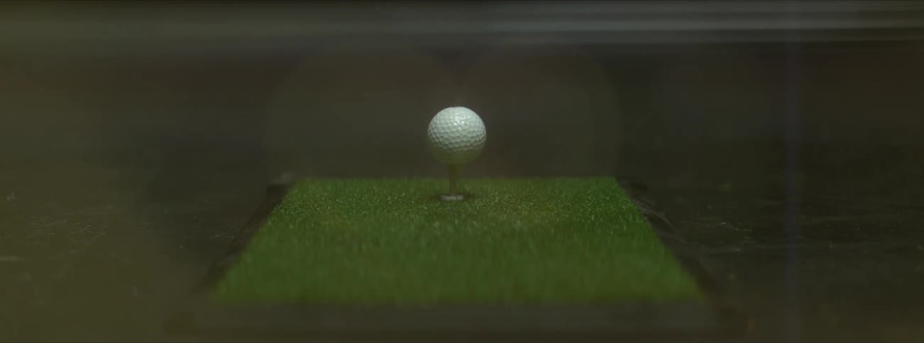 A golf ball is hit by a club and the tee spins off the patch of turf