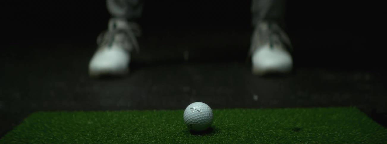 A golf club hits a ball off of a patch of green turf