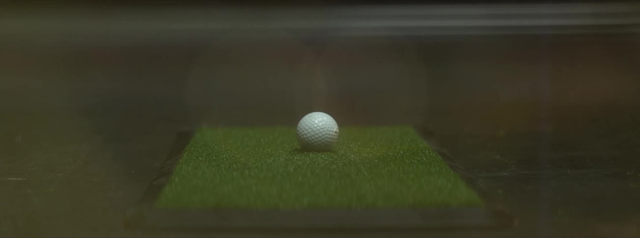 A close view of a golf ball being struck with a golf club while indoors