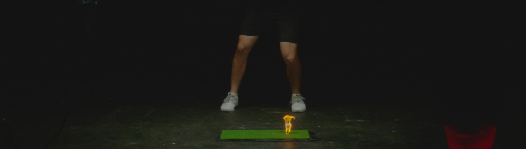 A man hits a golf ball that is sitting in flames