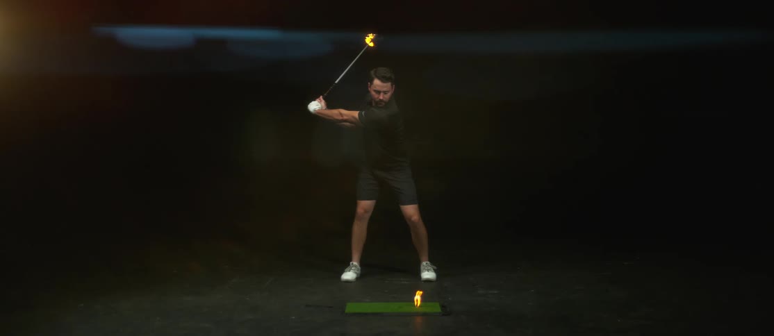 A man with a golf club swinging at a golf ball on fire