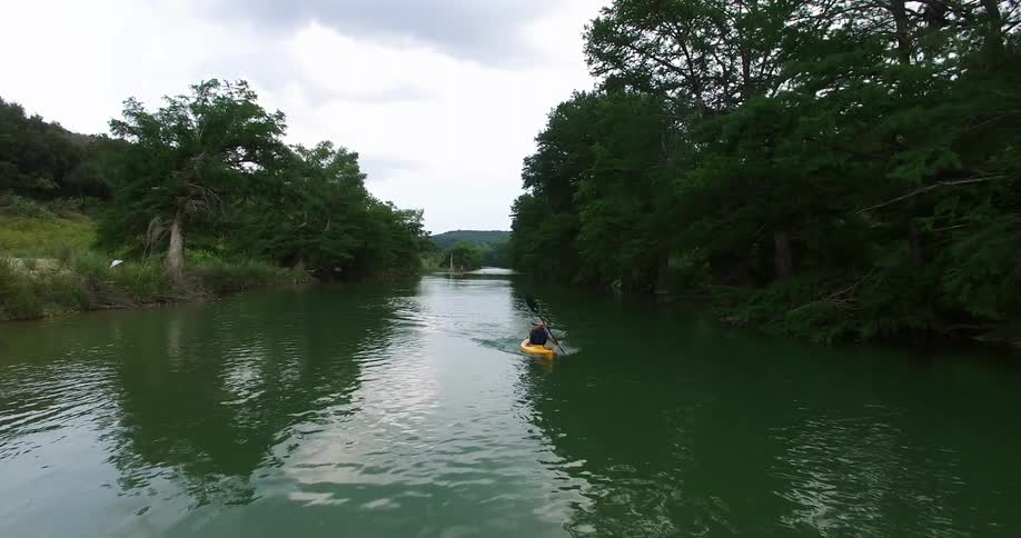 A person paddles down a river in a yellow kayak