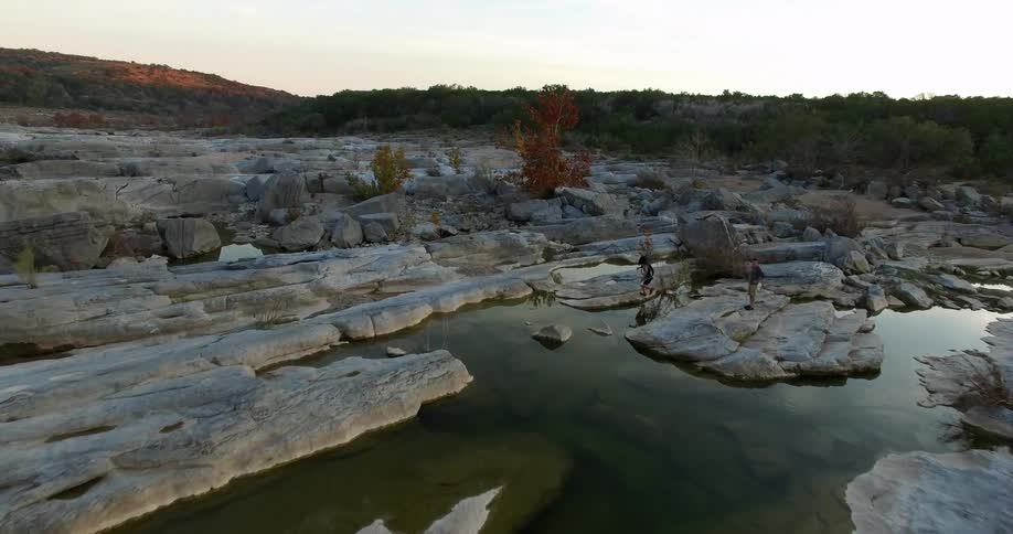 People are jumping over rocks near a stream below