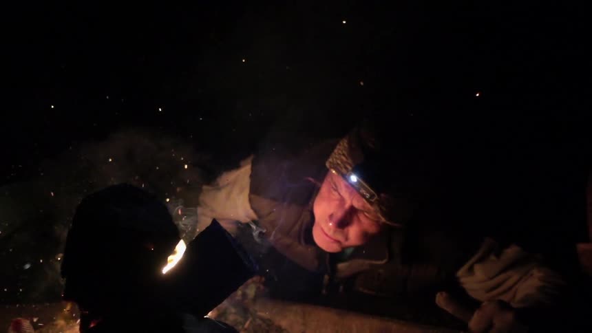 A man is leaning towards a fire at night