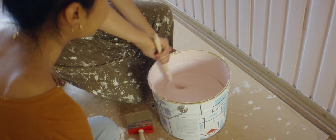 A woman is mixing paint with a paint stick