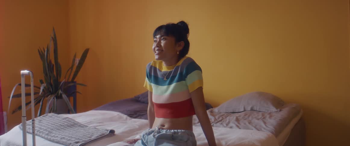 A woman sits on the bed and lays back to relax