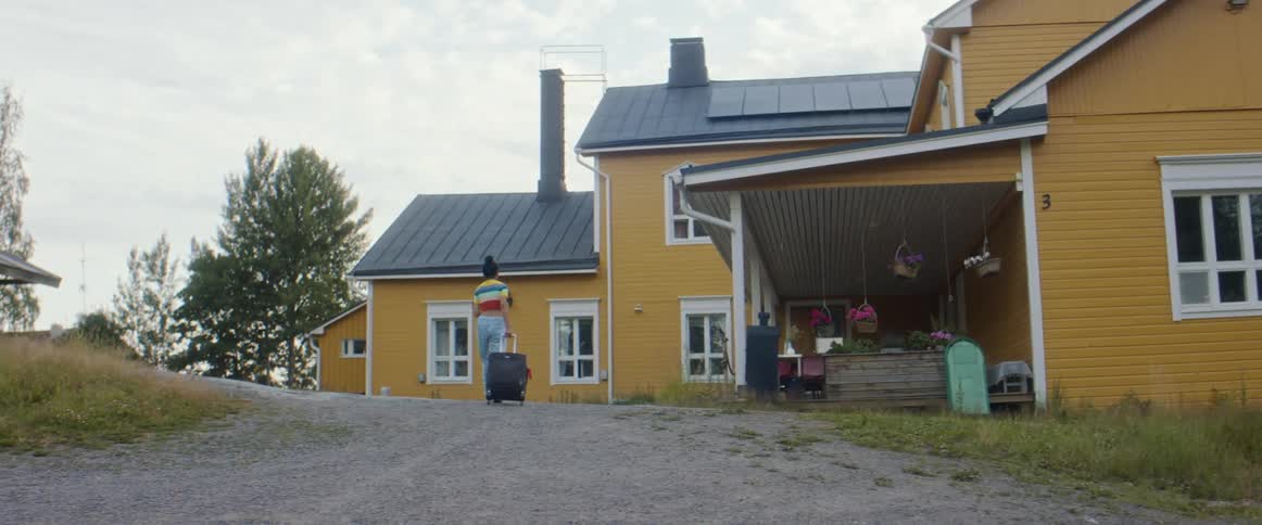 A woman pulls her luggage behind her as she walks up a driveway towards a house during the day