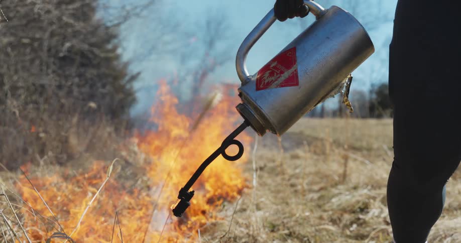 A person with gloves setting grass on fire with the sky and clouds in the background