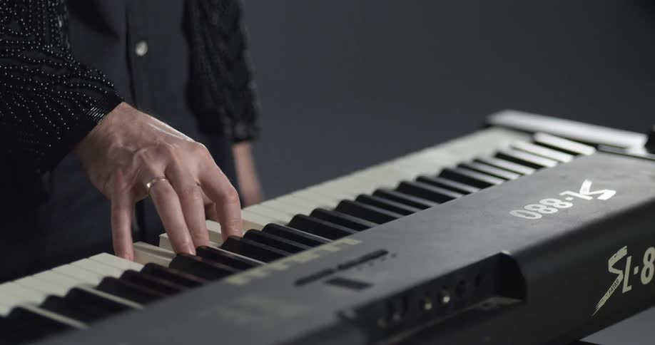 A person with a ring on their finger in a room playing a keyboard with a wall in the background