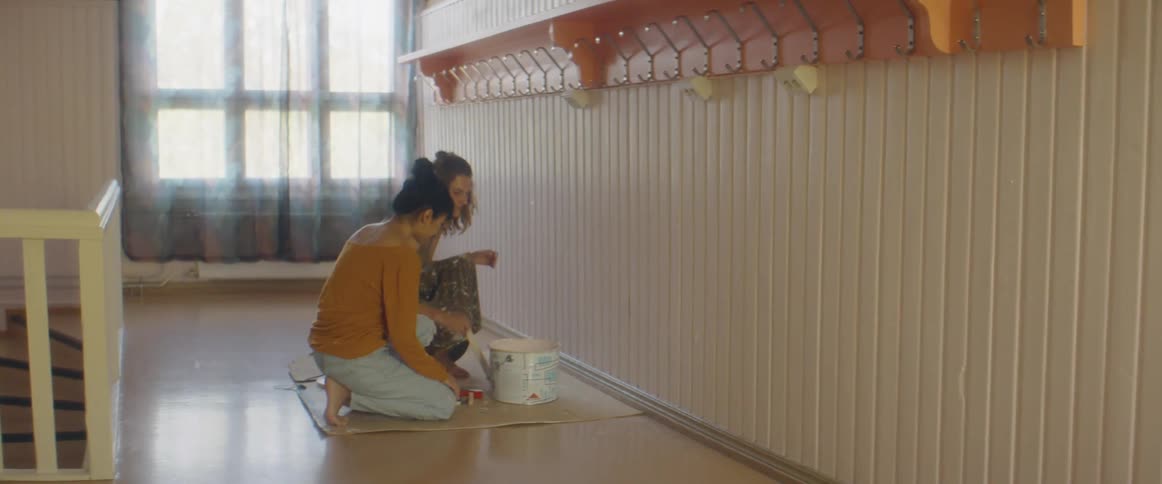 Two women open a paint can and stair the paint