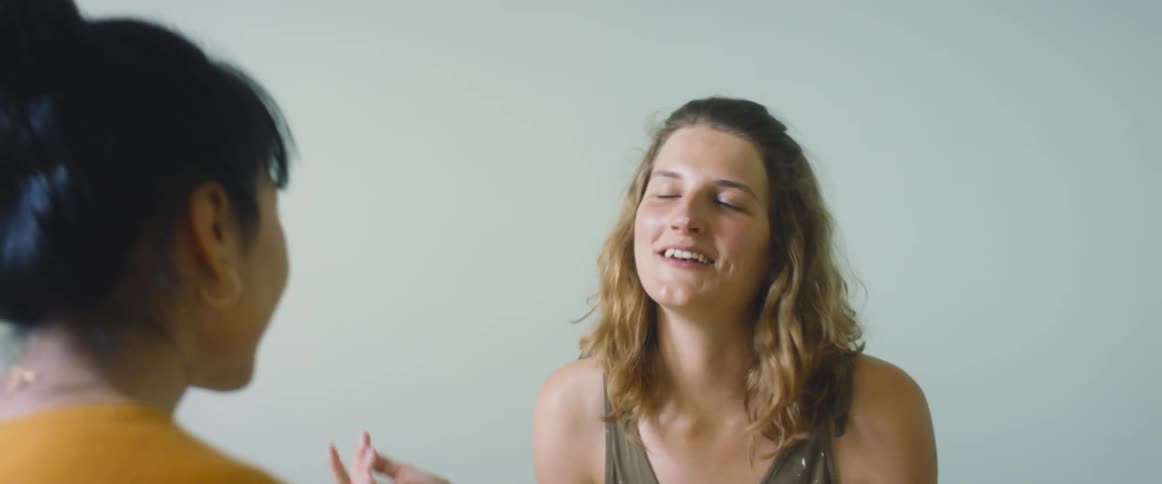 Two teenage girls talk and laugh and one leans forward to wipe paint off her friends nose