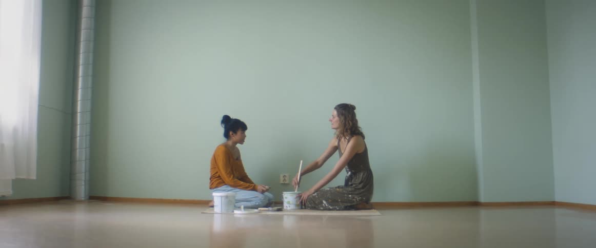 Two teenagers sit in an empty room and stir paint and talk