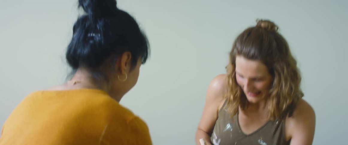 Two girls are playing with each other as they are painting on each other with a brush