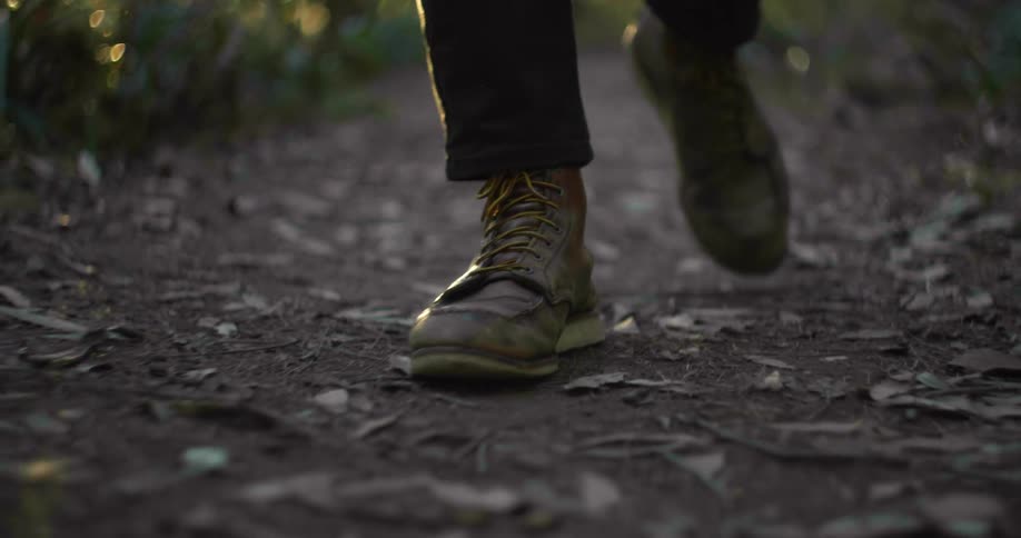 View of the boots of a man strolling along a pathway in a forest at dawn or dusk