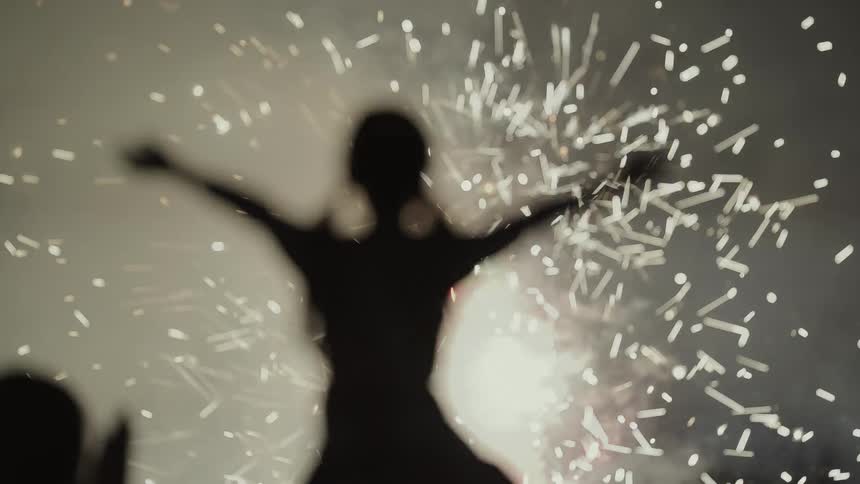 A young girl sitting on a mans shoulders holds her arms while as she watches fireworks exploding in the night sky