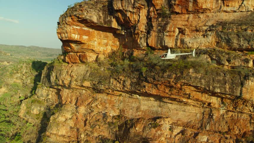 A helicopter climbs as it flies past a cliff in a canyon