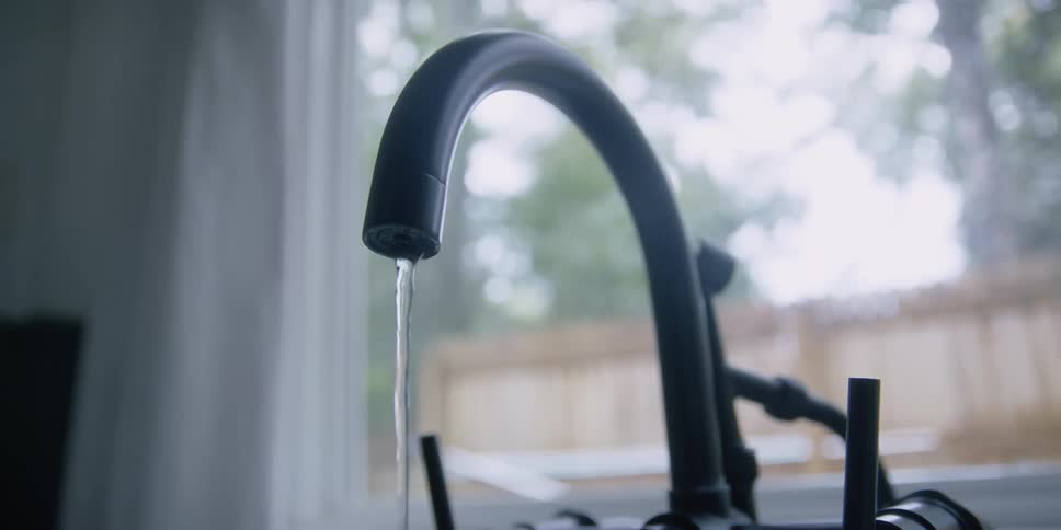 Water runs out of a black faucet near a window
