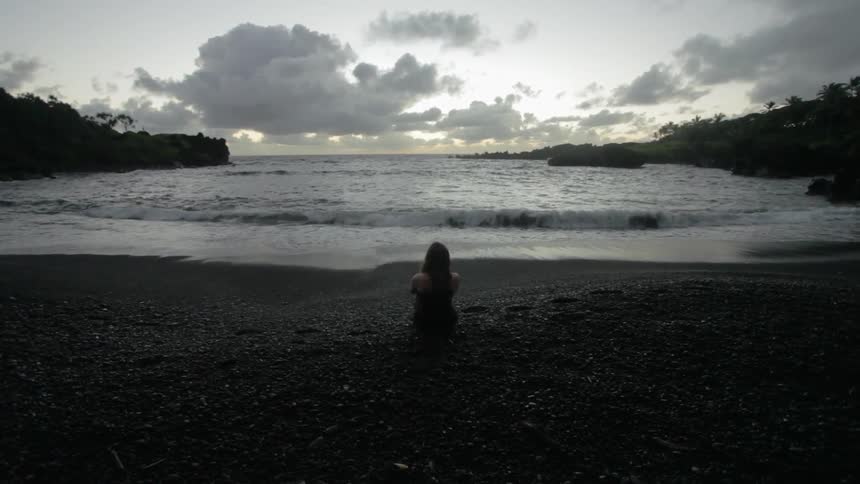 A person is sitting near the shore at sunset