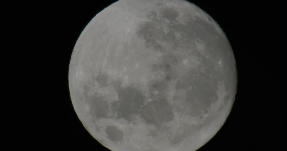 Various shades of white show details of lunar surface as moon sits in night sky