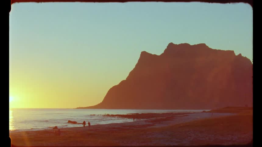 People walking on a beach near a mountain at sunset caught on vintage film