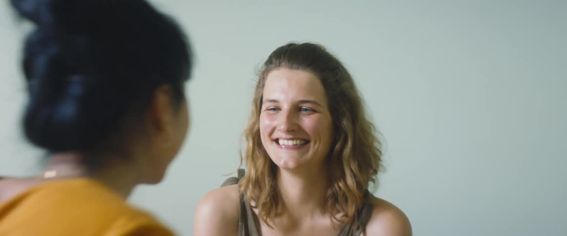One woman is playfully teasing another with trying to touch her face while indoors