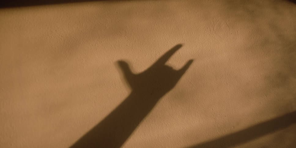 The shadow of a raised arm giving an i love you hand sign cast on a wall