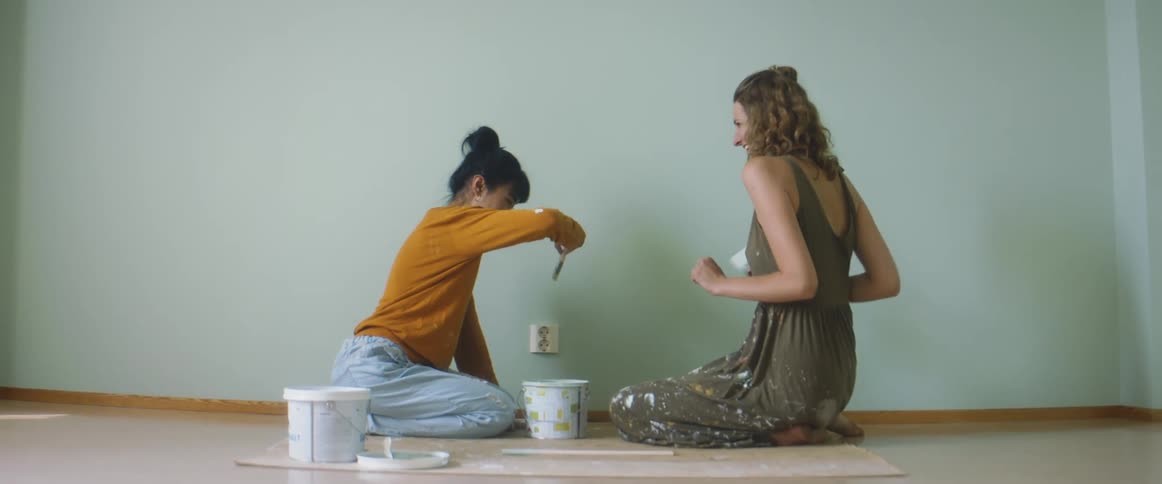 Two women play with brushes while painting the wall
