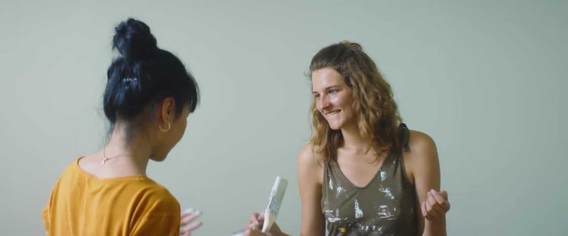 A pair of women playfully try to poke one another with paintbrushes covered in paint