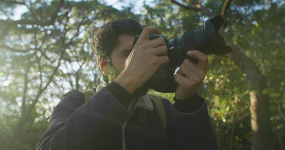 A photographer lifts his camera to take a photo in a woodland area during the day