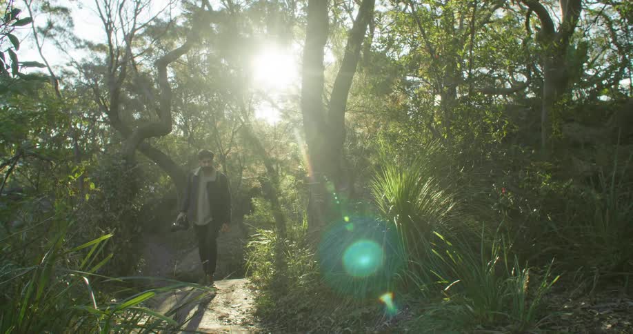 A man walking outdoors in a forest with a camera