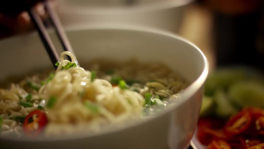 A person picking up noodles in a bowl with chopsticks on a table