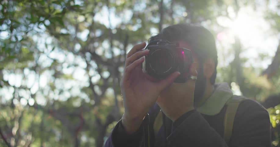 Young bearded man takes pictures with a camera on the forest at morning