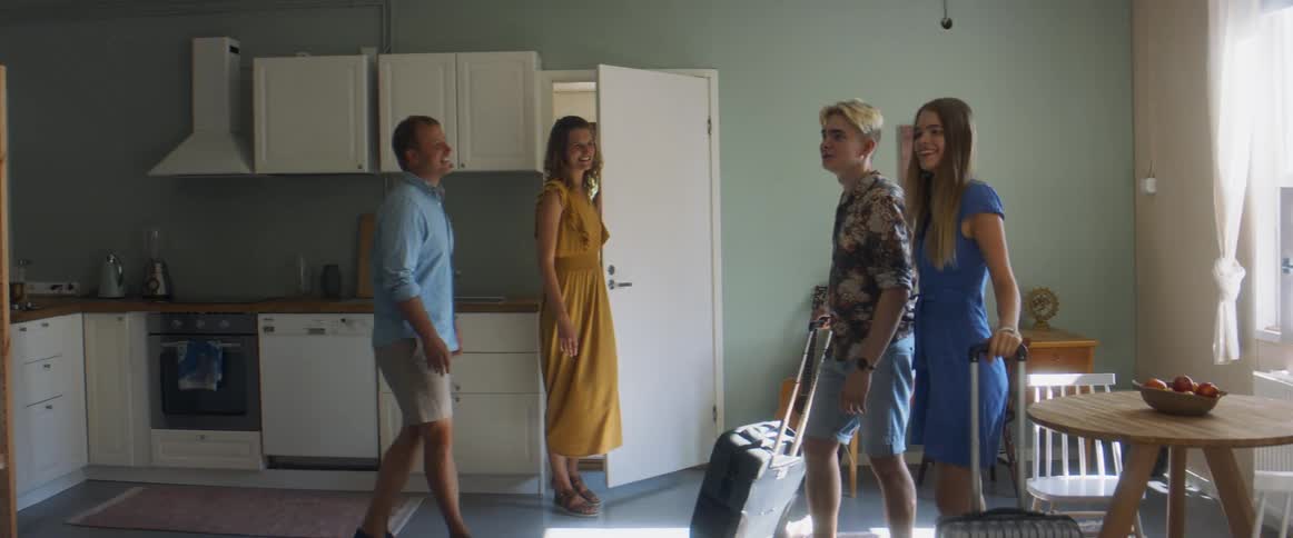 A young man and woman walk in to a room with suitcases and another man and woman follow behind them to show them the room