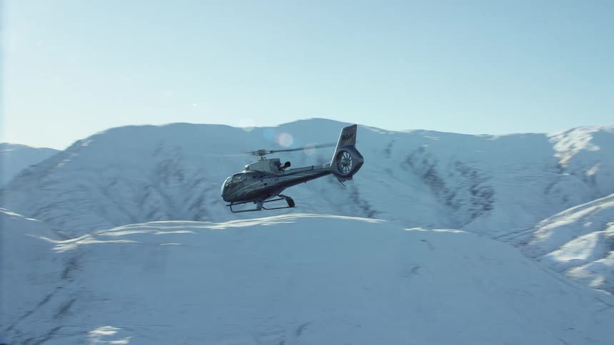A helicopter is flying near snow covered mountains