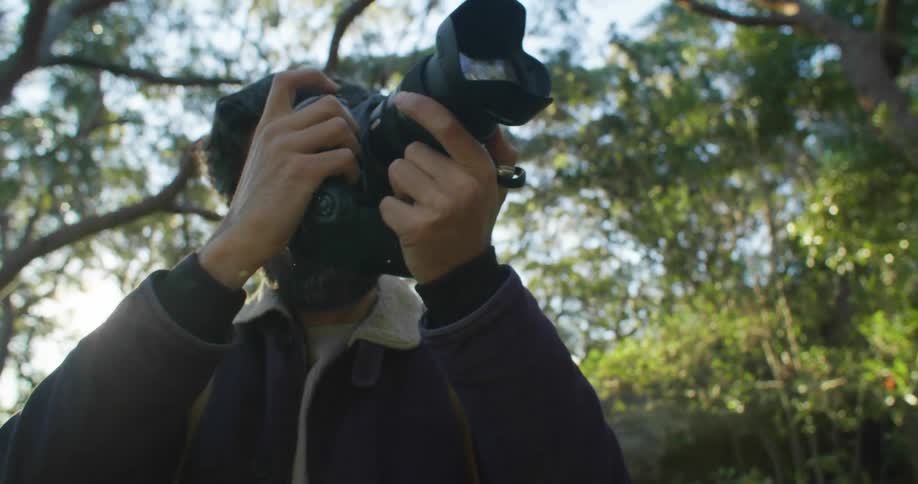 Photographer stands outdoors under trees taking photograph on sunny day