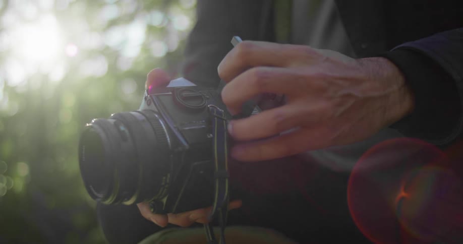 Photographer crouching on the forest floor loads a camera at morning