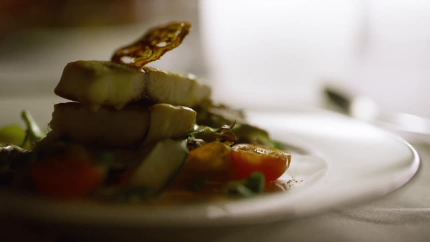 A persons hand puts down a carefully crafted plate of food on a table