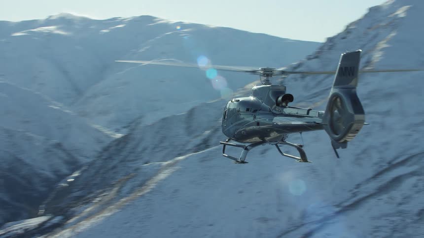 A helicopter with imw on it flies near snowcovered mountains near midday