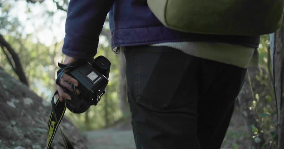 A photographer hikes through a woodland while carrying a camera during the day