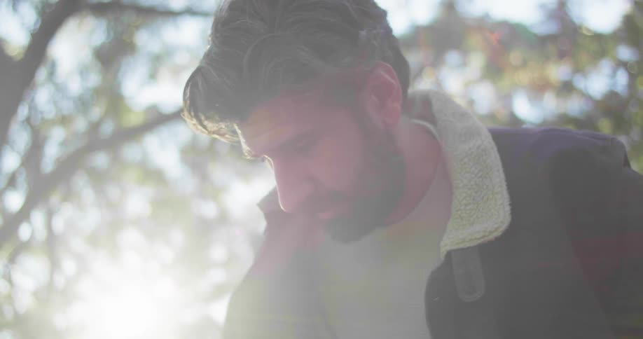 Bearded man takes a camera out of a backpack on a trail in the forest at morning