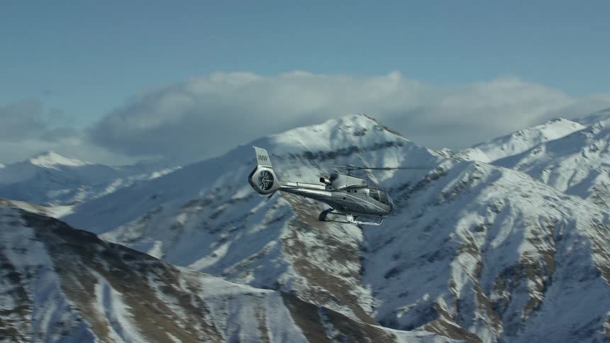 A helicopter is flying over snow covered mountains