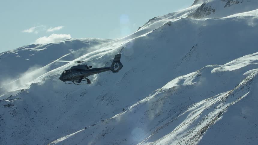 A helicopter is flying near snow covered mountains on a sunny day
