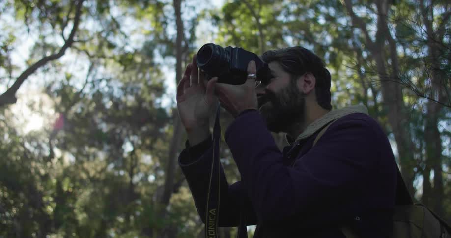 Young bearded man takes pictures on the forest at morning