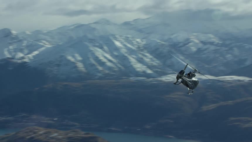 A helicopter is flying over a lake surrounded by snow covered mountains