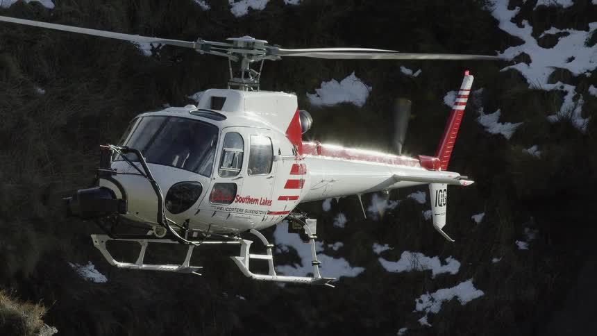 A helicopter flying in the air with a mountainside with snow and ice in the background