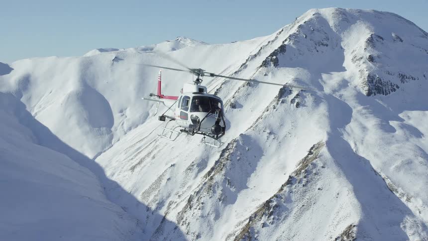 Helicopter flies over high snowy mountains