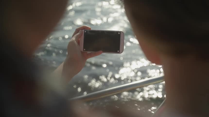 Two women take a selfie together with a smart phone as they stand near a railing on a boat