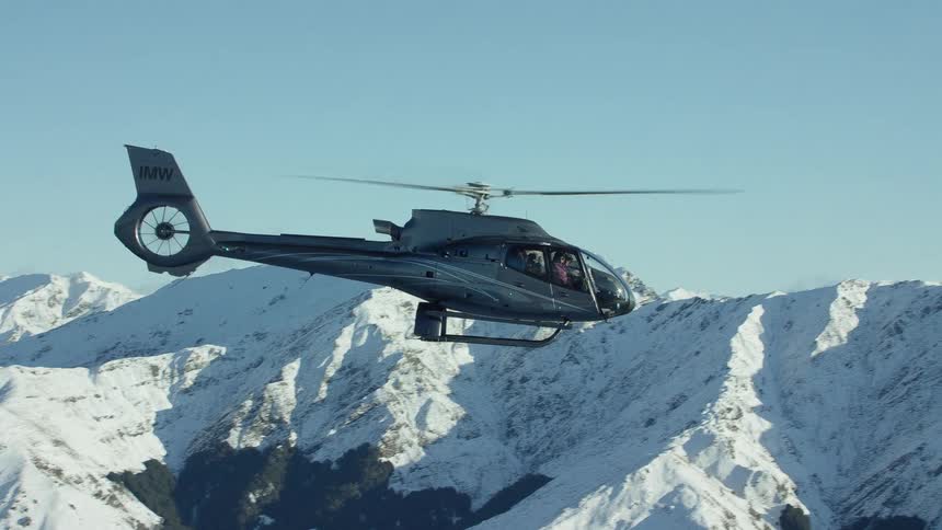 A helicopter flying in the sky with a snow covered mountain range the sky and clouds in the background