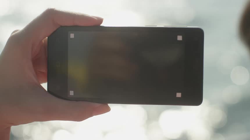 A person holding a phone with a replaceable screen in front of the ocean